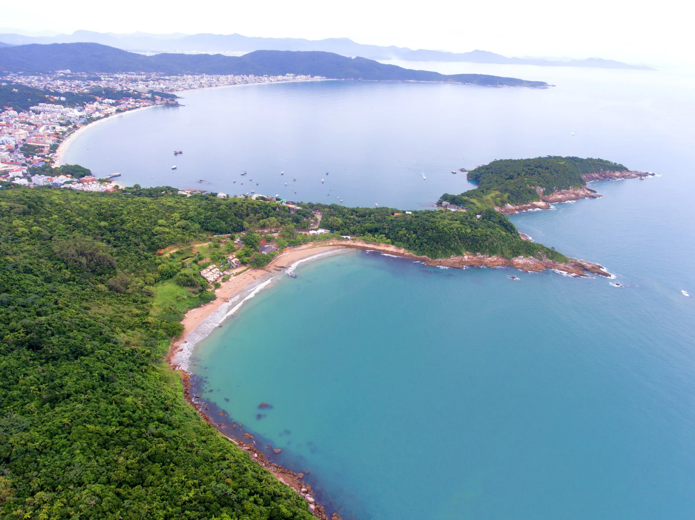 Vista aérea de la pequeña caleta de Sepultura rodeada de mata, con la punta rocosa y la playa de Bombinhas al fondo
